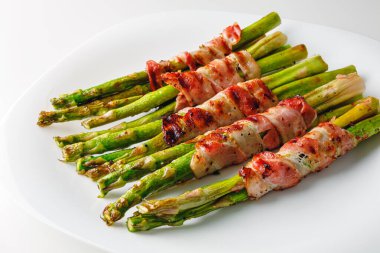 Grilled green asparagus wrapped with bacon. Asparagus baked with bacon and spices. Healthy food. Top view. Free space for your text. Bacon wrapped asparagus on white plate.