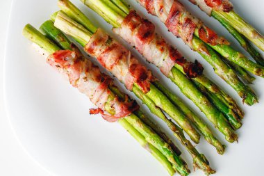 Grilled green asparagus wrapped with bacon. Asparagus baked with bacon and spices. Healthy food. Top view. Free space for your text. Bacon wrapped asparagus on white plate.