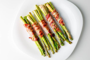 Grilled green asparagus wrapped with bacon. Asparagus baked with bacon and spices. Healthy food. Top view. Free space for your text. Bacon wrapped asparagus on white plate.
