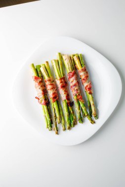 Grilled green asparagus wrapped with bacon. Asparagus baked with bacon and spices. Healthy food. Top view. Free space for your text. Bacon wrapped asparagus on white plate.
