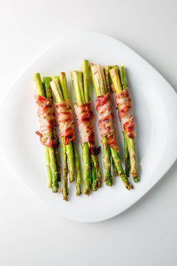 Grilled green asparagus wrapped with bacon. Asparagus baked with bacon and spices. Healthy food. Top view. Free space for your text. Bacon wrapped asparagus on white plate.