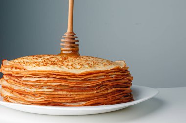 Close-up delicious pancakes, with fresh mint and honey on a light background. With copy space. Sweet maple syrup flows from a stack of pancake.
