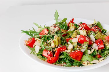 Vegetable arugula salad with iceberg lettuce, romaine and radicchio in a metal bowl on white background. Top view, copy space. Avocado, cucumber, tomatoes cherry, sesame seeds, flax seeds, olive oil