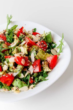 Vegetable arugula salad with iceberg lettuce, romaine and radicchio in a metal bowl on white background. Top view, copy space. Avocado, cucumber, tomatoes cherry, sesame seeds, flax seeds, olive oil