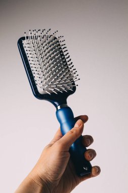 Blue hair comb in hand on white and light gray background. Isolated. Copy space. Hairbrush comb.