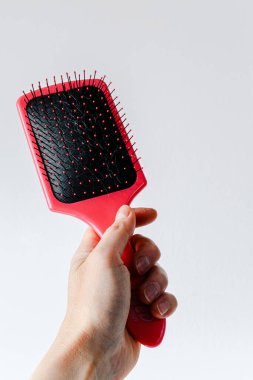 Pink hair comb in hand on white and light gray background. Isolated. Copy space. Hairbrush comb.