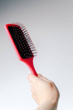Pink hair comb in hand on white and light gray background. Isolated. Copy space. Hairbrush comb.