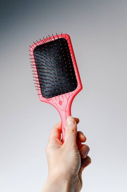 Pink hair comb in hand on white and light gray background. Isolated. Copy space. Hairbrush comb.