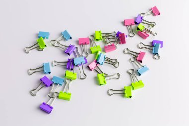 Colorful metal binder clips - office supply on light grey and white background.
