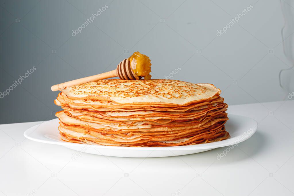 Close-up delicious pancakes, with fresh mint and honey on a light background. With copy space. Sweet maple syrup flows from a stack of pancake.