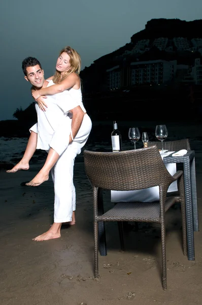ビーチでロマンチックなディナーを祝う白い服を着た若いカップル — ストック写真