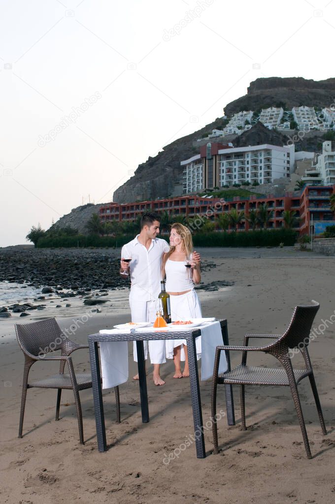 Young couple dressed in white celebrating a romantic dinner on the beach