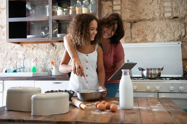在网上的平板电脑上看她的食谱时 她正在和女儿一起烹调卷曲的女食 — 图库照片