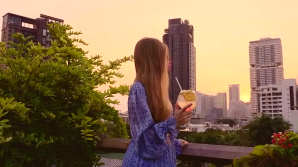 Młoda kobieta w sukni Holding Cocktail na tarasie baru na dachu podczas zachodu słońca — Wideo stockowe