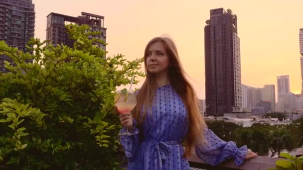 Junge schöne Frau im eleganten Kleid hält Cocktail auf Dachterrasse — Stockvideo