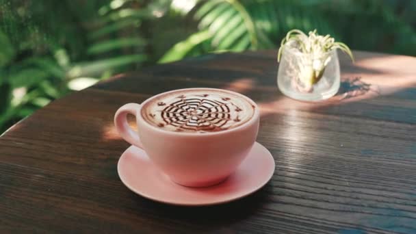 Coupe de cappuccino chaud avec Latte Art sur table en bois avec verdure tropicale — Video