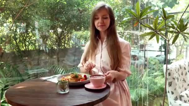 Χαρούμενη χαμογελαστή γυναίκα κάθεται στο καφέ, πίνοντας καφέ από το ροζ κύπελλο στο Cozy Cafe — Αρχείο Βίντεο