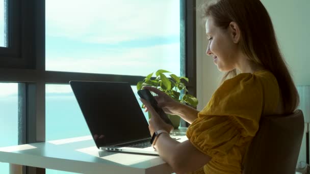 Jeune heureuse joyeuse femme d'affaires mignonne assise à l'intérieur au bureau à domicile, vue sur la mer — Video