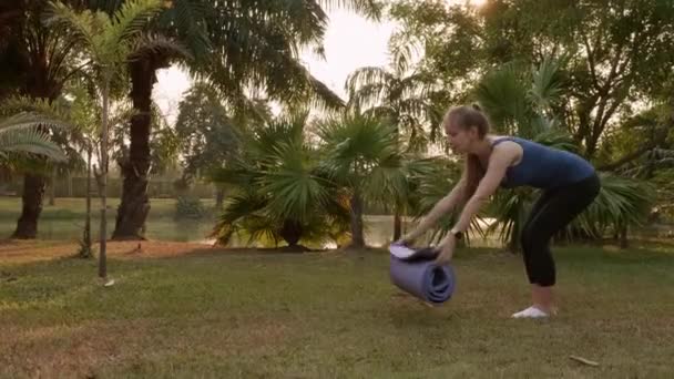 Kobieta przygotowuje się do jogi, umieść matę na zielonym trawniku w Outdoor Park — Wideo stockowe