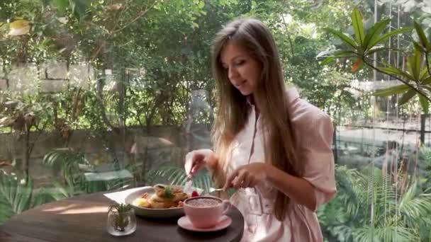 Felice donna sorridente seduta nel caffè, mangiare frittelle fresche con City Street — Video Stock