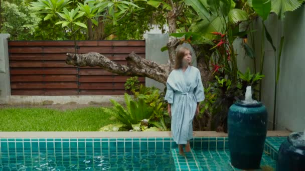 Atrakcyjna kobieta w szlafroku spaceruje wzdłuż krawędzi basenu w pokoju hotelowym — Wideo stockowe