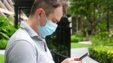 Covid-19 Coronavirus 'a karşı koruyucu tıbbi maskeli adam, akıllı telefon kullan.