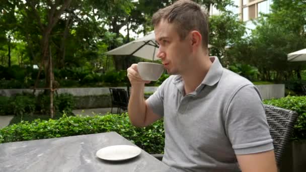 Hombre beber taza de café de capuchino, sentarse en el restaurante al aire libre o cafetería en el parque — Vídeos de Stock