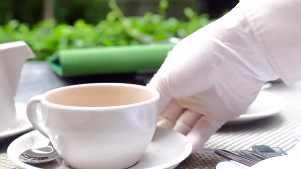 Ober hand in rubber handschoen zet restaurant klant orde koffie kopje op tafel — Stockvideo