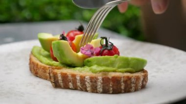 Sabah vejetaryen yemeği. Erkek eli çavdar ekmeğini püre ve dilimlenmiş avokado ile keser.