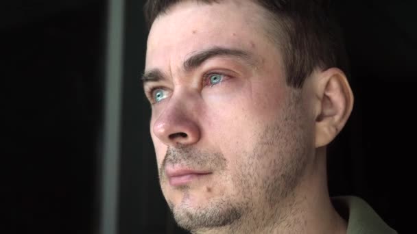 Smutny mężczyzna z jednym czerwonym i zapalonym okiem wyglądającym przez okno — Wideo stockowe