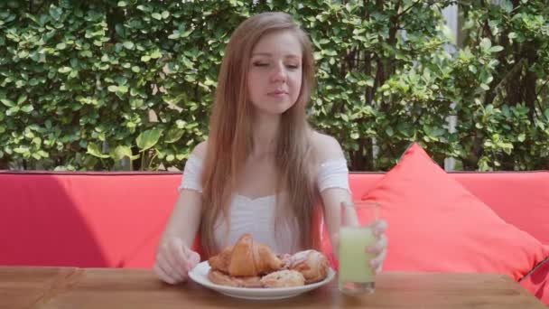 Junge Frau isst Frühstück oder Mittagessen im Restaurant mit Croissant, Gebäck, Saft — Stockvideo