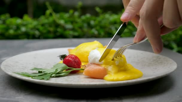Las manos masculinas cortan huevos benedictos y comen, el hombre desayuna, almuerza o cena en la cafetería — Vídeo de stock