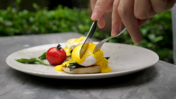 Man äter läckra pocherade ägg med flytande ägg Yolk i Green Outdoor Cafe — Stockvideo