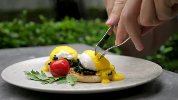 Man Jedzenie pyszne jajka gotowane z płynnym żółtkiem jaj w zielonej kawiarni na świeżym powietrzu — Wideo stockowe