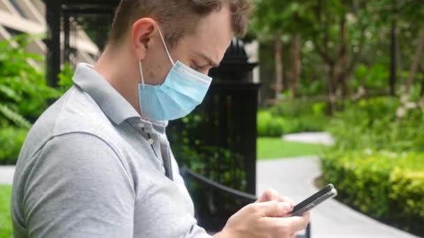 Grappige man in het gezicht masker kijkt in mobiele telefoon, het lezen van onverwacht nieuws, verrast — Stockvideo