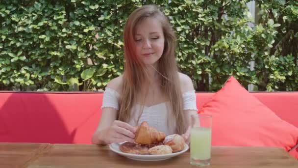 Mladá krásná žena si vychutnat snídani, jíst čerstvé pekárny v open-air restaurace — Stock video