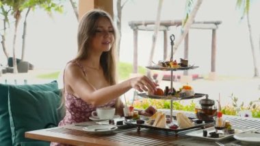 Açık hava restoranında tatlı yiyen ve tatilde palmiye ağaçları olan bir kadın.