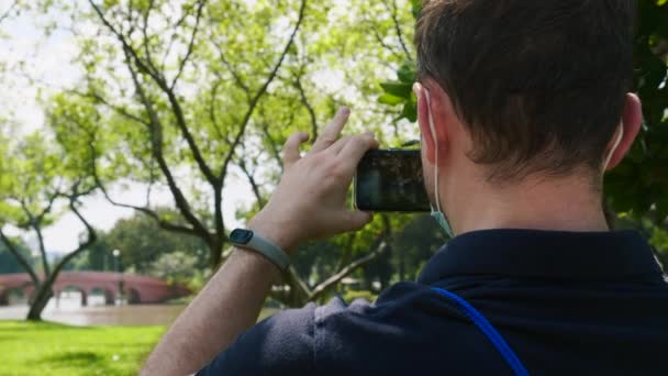 Yüz maskesi altında seyahat blogcusu veya vlogger parkta cep telefonunda video kaydı — Stok video