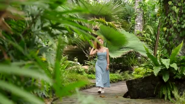 Νεαρή ταξιδιωτική γυναίκα στο τροπικό δάσος περπατώντας, αγγίζοντας το φύλλο φοίνικα — Αρχείο Βίντεο