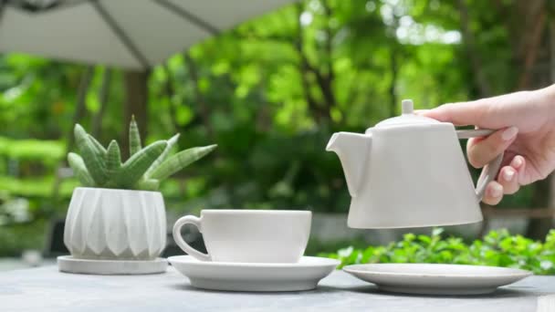 Mano femenina vertiendo té caliente de tetera a taza en restaurante al aire libre, terraza cafetería — Vídeo de stock