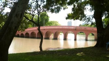 Arka planda göleti, köprüsü ve modern binaları olan kamu parkı, Bangkok