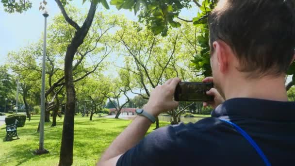 Чоловічий туристичний блогер записує відео на мобільний телефон, стоячи на природі — стокове відео
