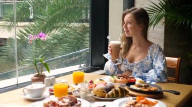 Genç bir kadın kahvaltıda lüks otel restoranında pipetle soğuk kahve içer.
