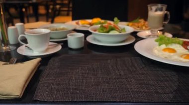 Garson lokantada yemek servisi yapıyor, erkek eli masaya tabak koyuyor.