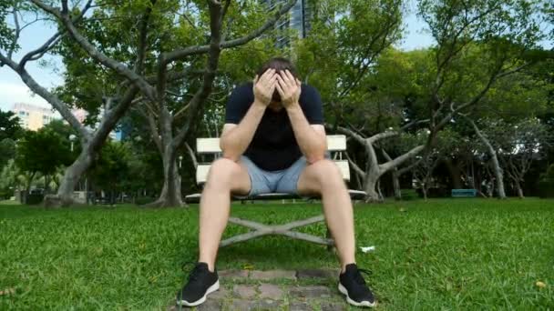 Droevige depressieve man voelt zich slecht, het aanraken van hoofd met de handen, zitten op bank in het park — Stockvideo