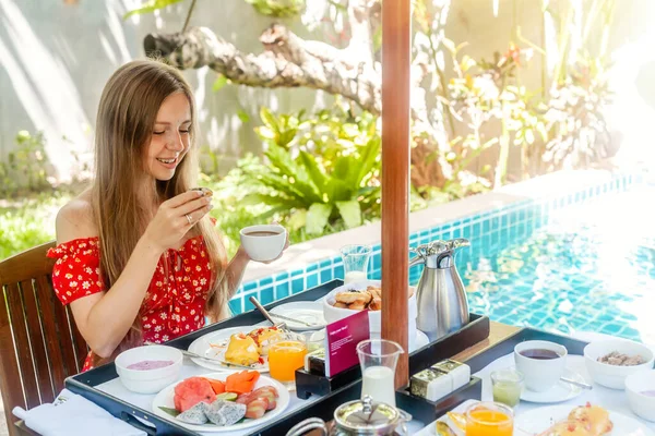 Mujer joven desayunar, beber café o té en la piscina con agua azul en la villa — Foto de Stock