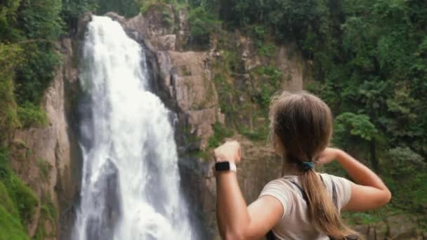 Jovem mulher de viagem feliz olhando em grande cachoeira e levantou as mãos — Vídeo de Stock