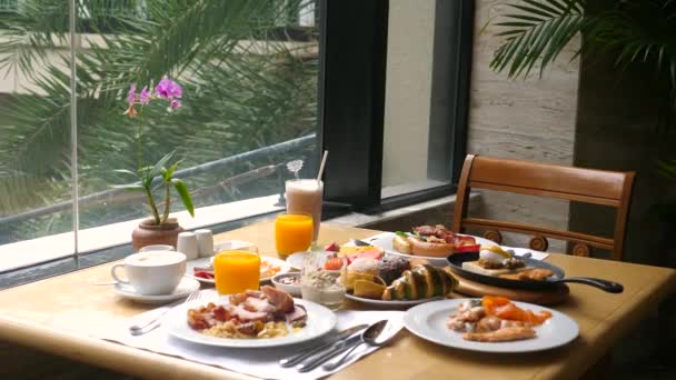 Otel kahvaltısı. Açık büfeden çeşitli yiyeceklerle panoramik pencerenin yanındaki masa — Stok video
