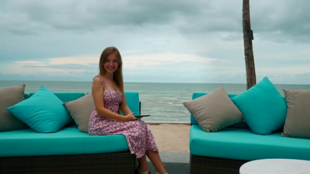 Amusant femme souriante heureuse en robe assis avec téléphone mobile sur le canapé près de la plage — Video