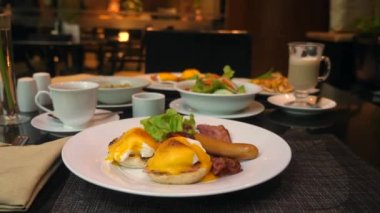 Garson kahvaltı masasında kızarmış yumurta, sosis, domuz pastırması ve kahveyle servis yapıyor.